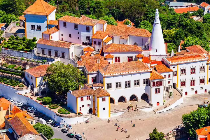 Aerial view of Sintra National Palace with its iconic chimneys and lush gardens, featured in a full-day tour including Pena Palace and Cascais.