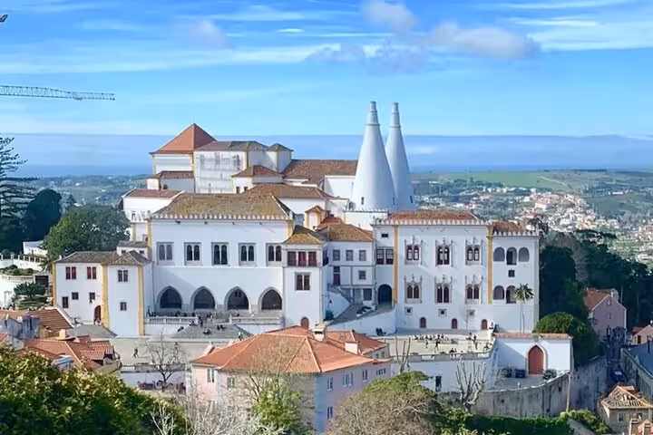 Majestic view of Sintra National Palace under a clear blue sky, showcasing its iconic twin chimneys and historic architecture.