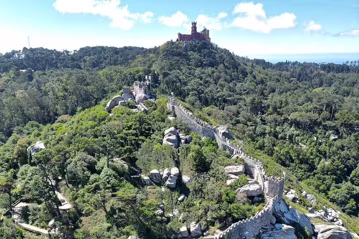 Aerial view of lush Sintra hills with the iconic Pena Palace and ancient stone walls, perfect for a small-group day tour adventure.