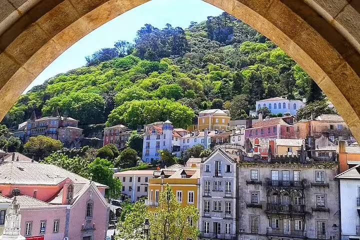 Picturesque view of Sintra's colorful hillside homes framed by a stone arch, showcasing vibrant architecture and lush greenery.