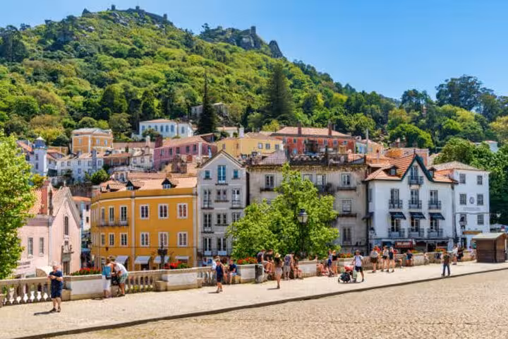 Colorful hillside village in Sintra with lush greenery and tourists exploring cobblestone paths.