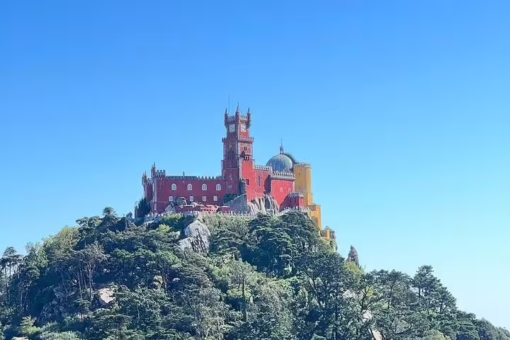 Colorful Pena Palace perched atop lush hills under a clear blue sky, featured in a Sintra half-day guided tour.