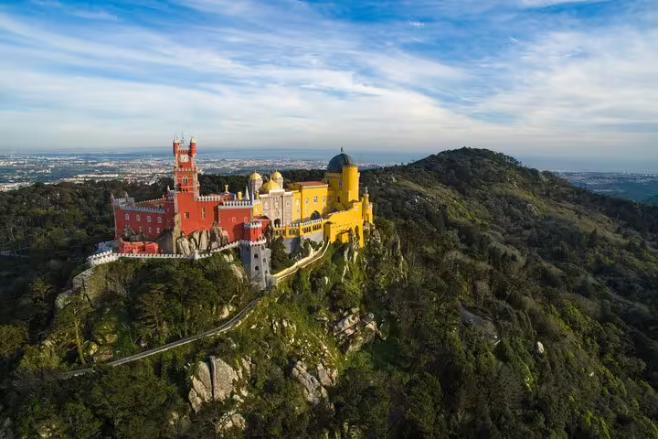 Aerial view of Sintra's colorful Pena Palace atop lush hills, a highlight of the guided tour with Moorish Castle tickets.