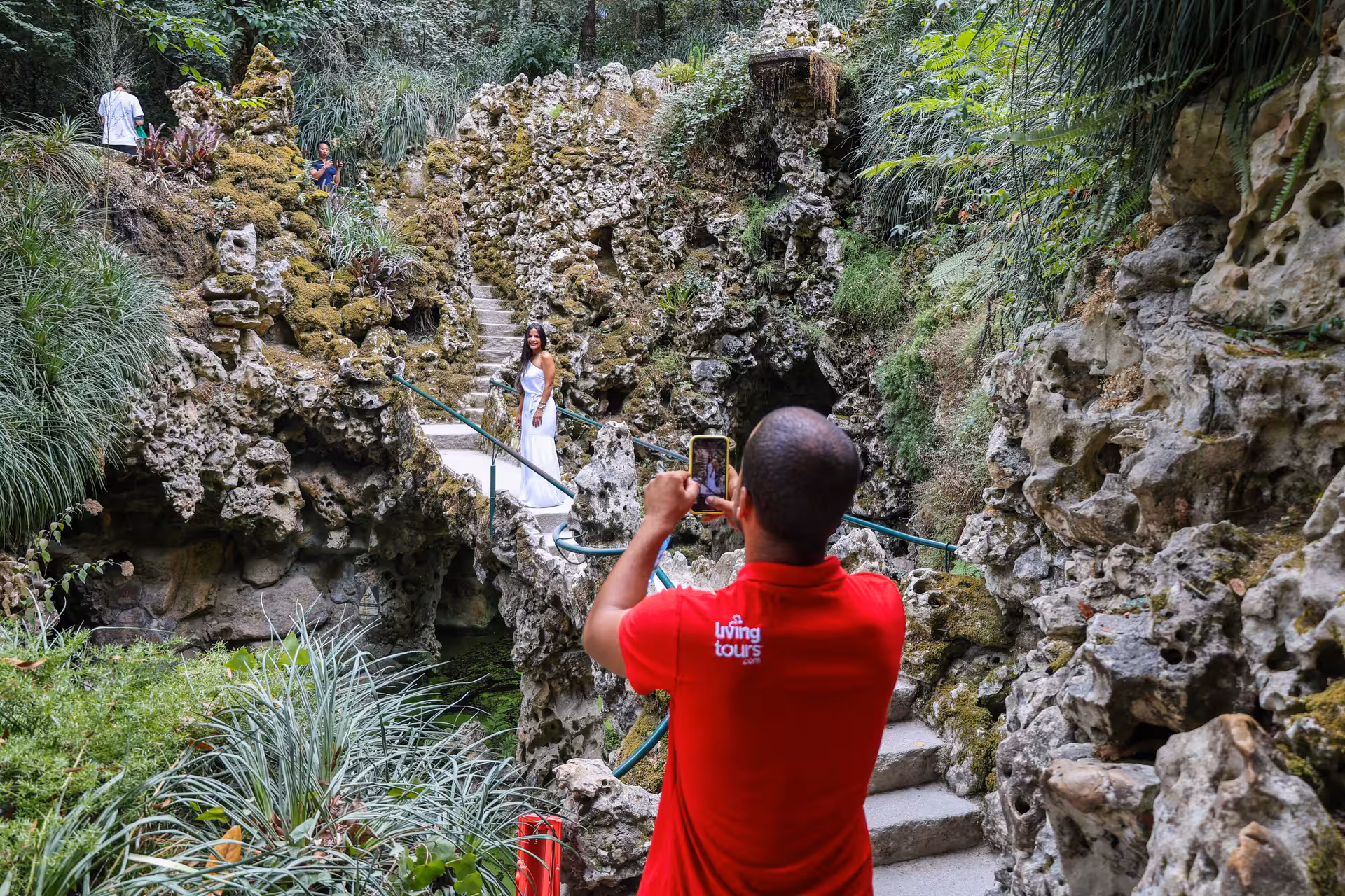 Tourists explore moss-covered rock formations at Quinta da Regaleira, Sintra, capturing scenic moments.