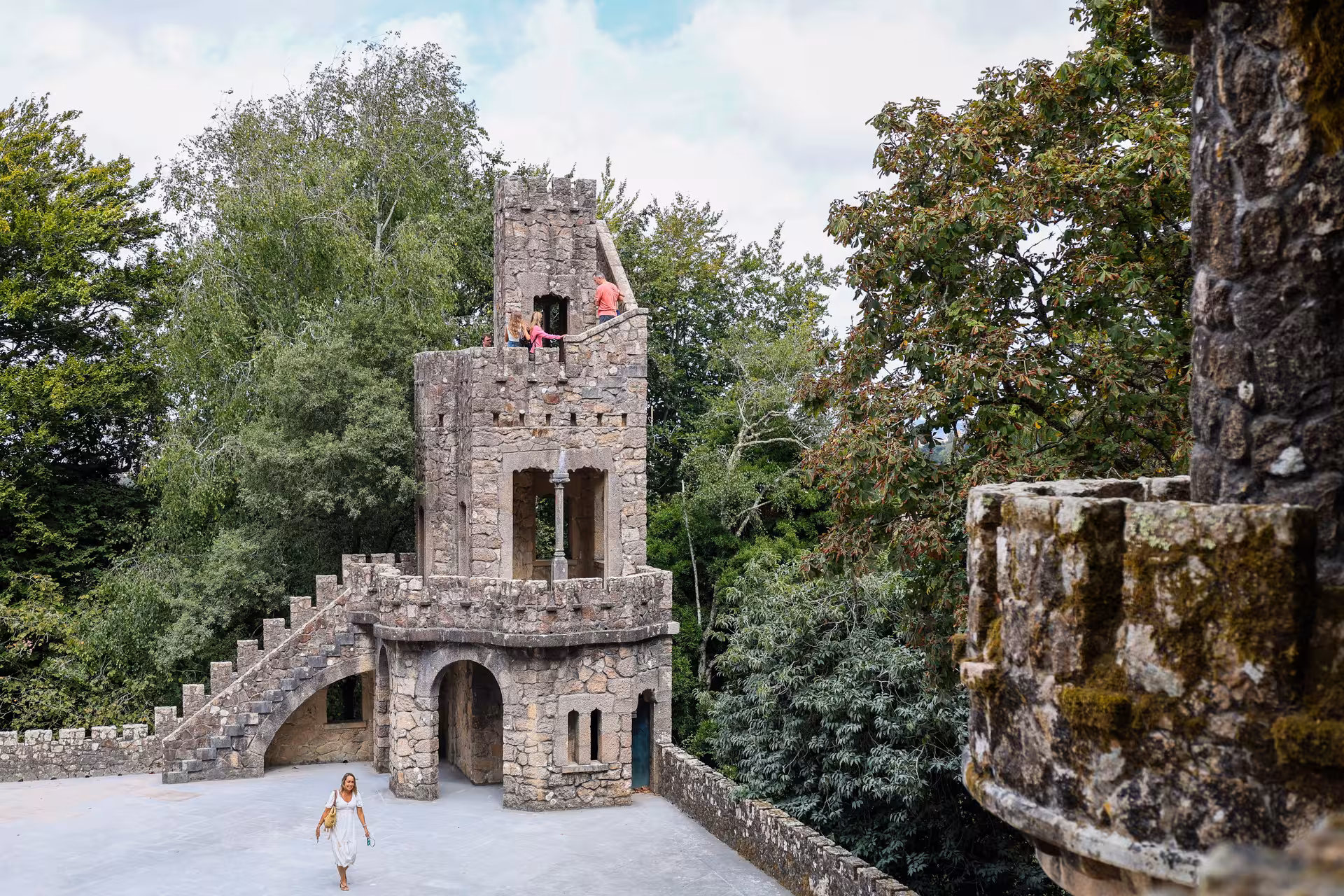 Tourists explore the historic stone tower at Quinta da Regaleira, surrounded by lush greenery on Sintra tour.