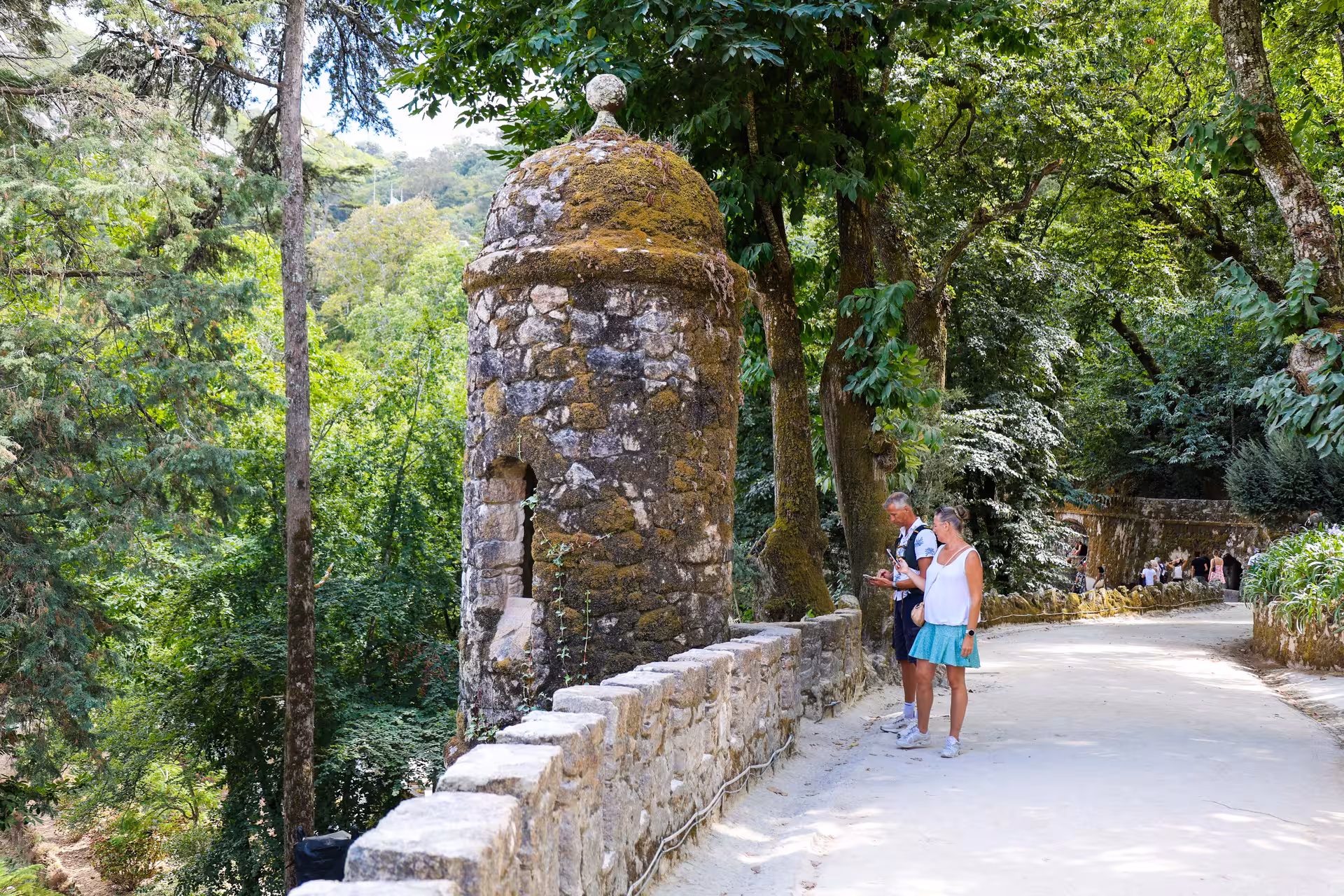 Visitors admire a stone turret surrounded by lush greenery at Quinta da Regaleira, part of a Sintra day tour.