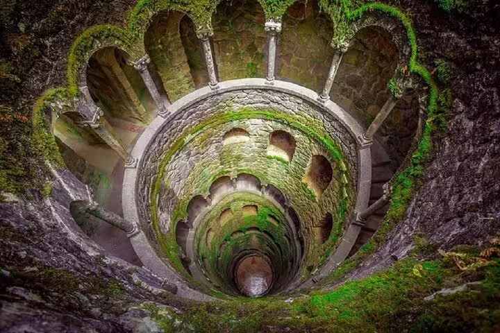 The mystical Initiation Well in Sintra's Quinta da Regaleira, showcasing its spiral staircase and moss-covered walls.