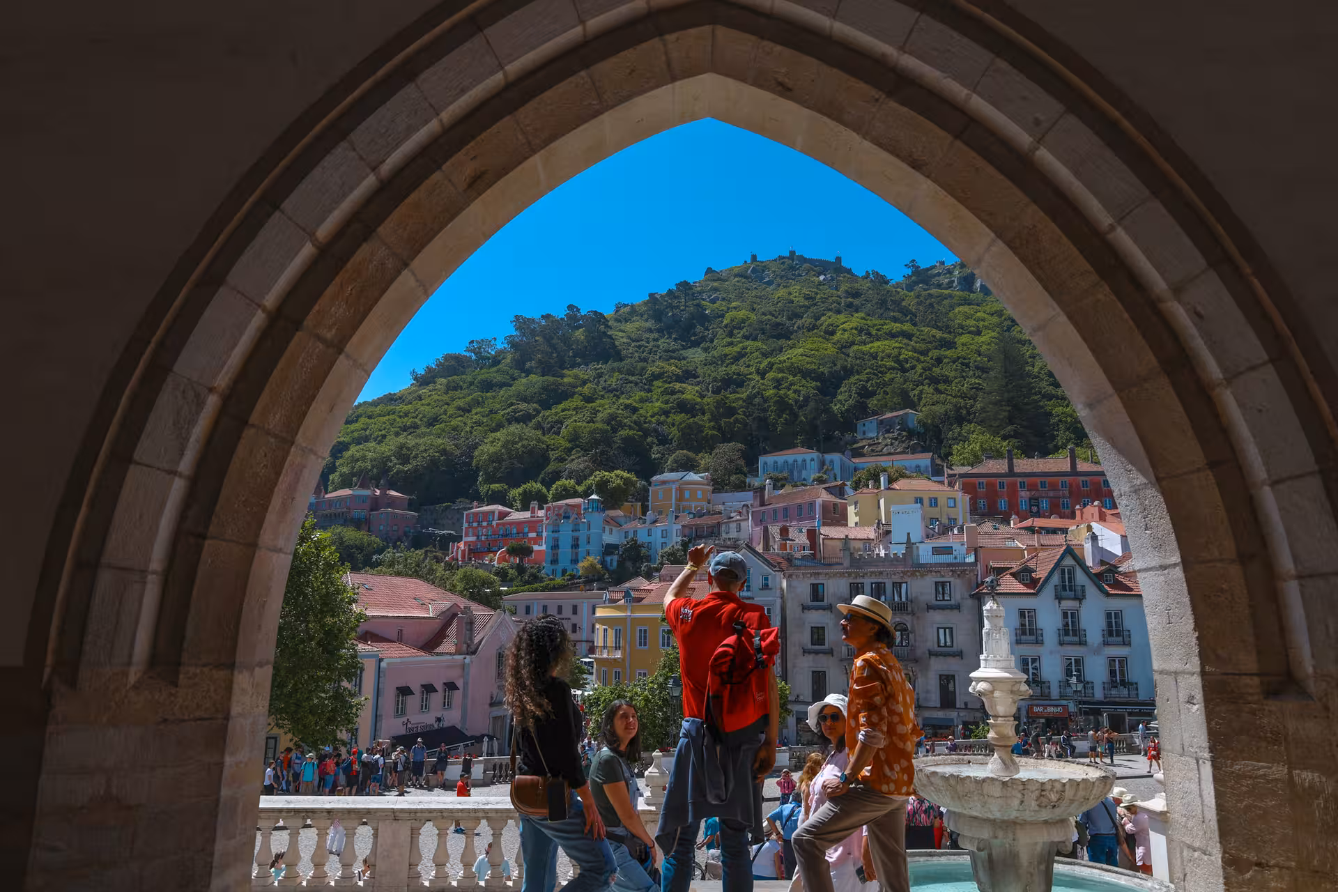 Tourists enjoy a scenic view of Sintra's colorful hillside architecture framed by a historic archway.