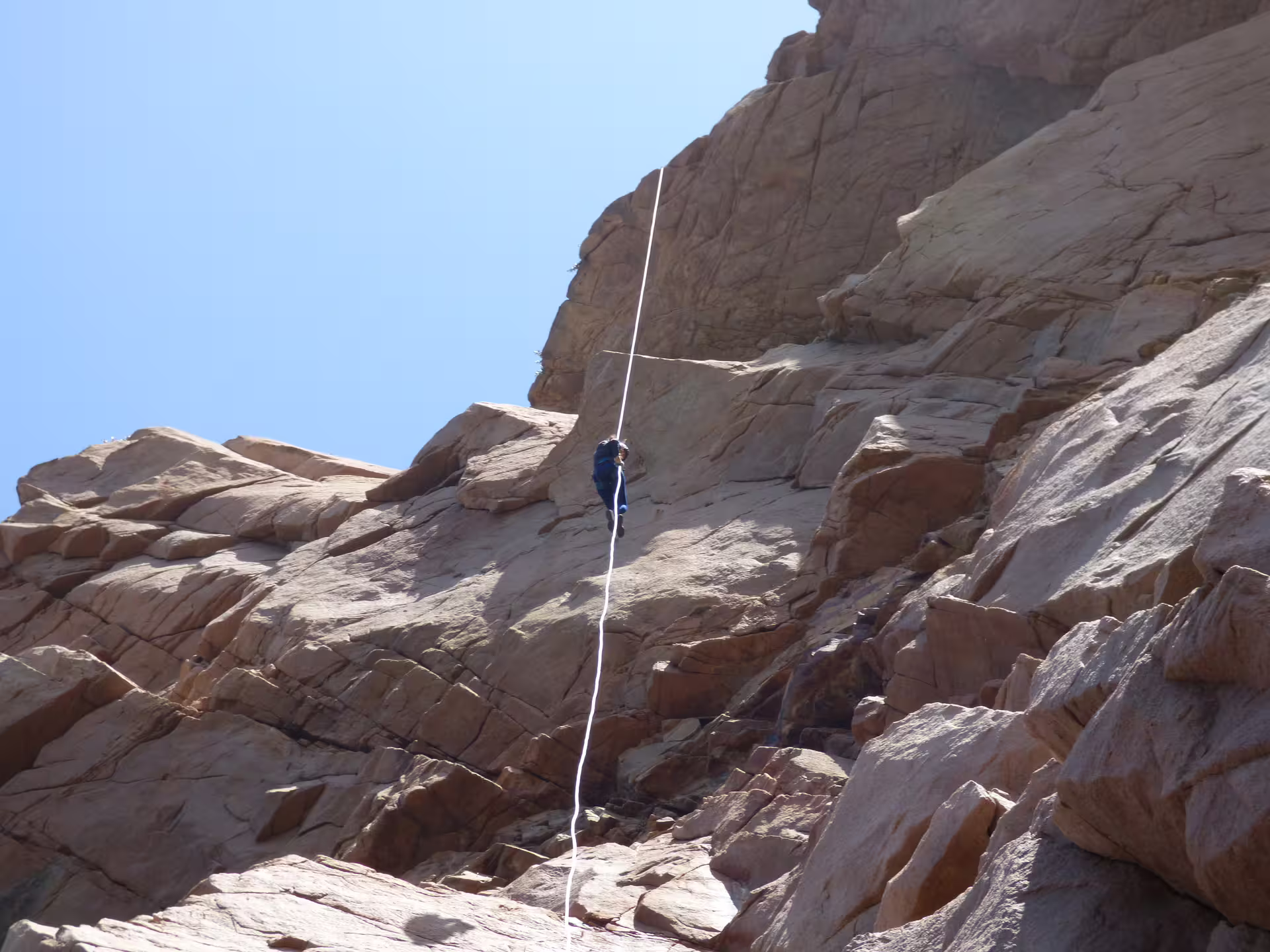 Adventurer rappelling down a rugged rock face under clear blue skies on the Sintra Rappelling Circuit experience.