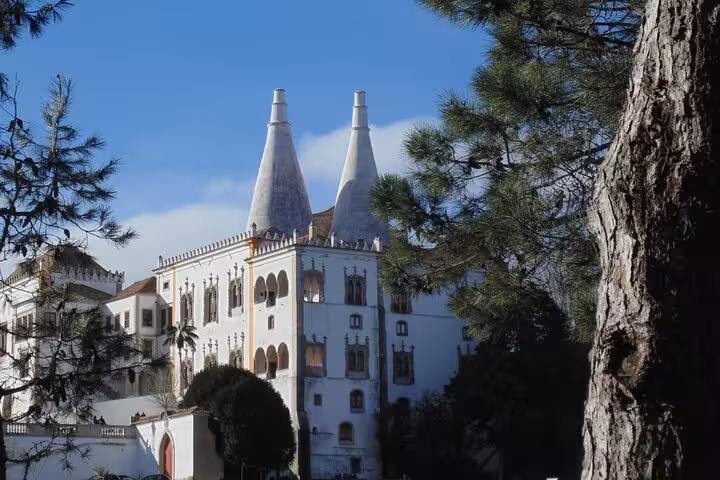Discover the enchanting architecture of Sintra's National Palace surrounded by lush greenery and blue skies.