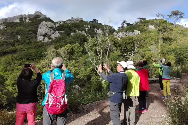 Tourists capturing scenic views of lush greenery and rocky landscapes during a Sintra, Roca, and Cascais full-day private tour.