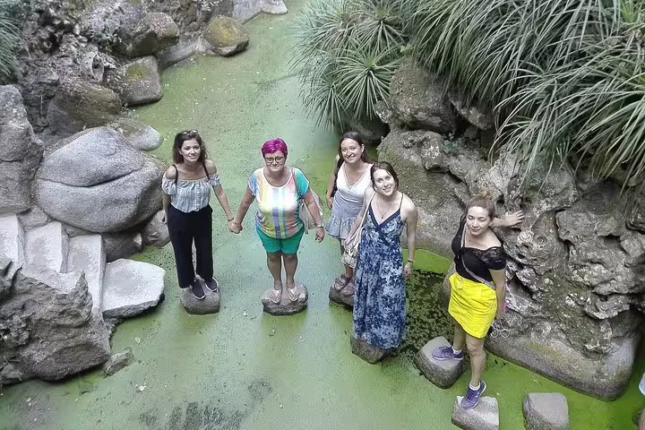 Group of tourists enjoying a serene moment on stepping stones surrounded by lush greenery during a Sintra, Roca, and Cascais tour.