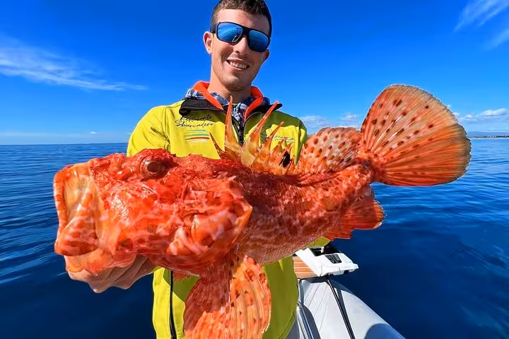 Smiling local fisherman holding a large vibrant red scorpionfish caught during a guided fishing tour in Siracusa Sicily