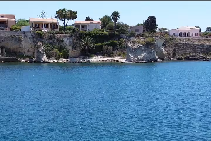 Scenic Siracusa coastline with crystal-clear blue waters, rocky cliffs, and Mediterranean villas on a guided fishing tour