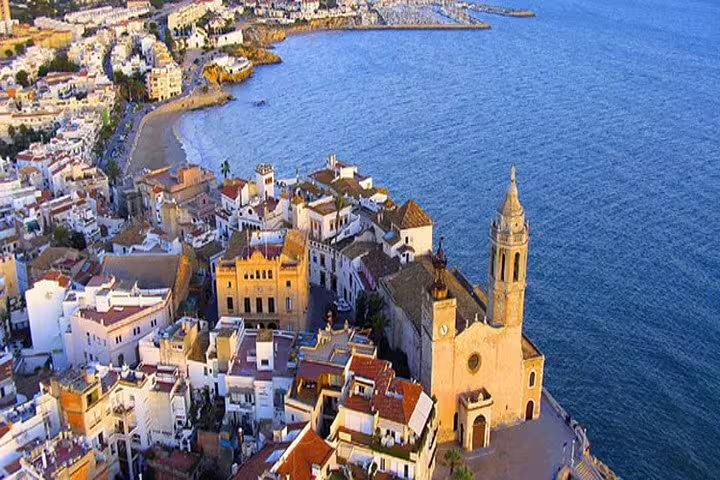 Aerial view of Sitges coastline featuring iconic church and vibrant rooftops along the Mediterranean Sea.