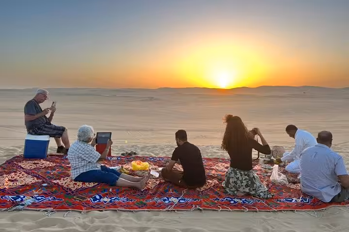 Sunset picnic on Sahara dunes during Siwa Oasis private 3-day safari, desert camp rug and travelers