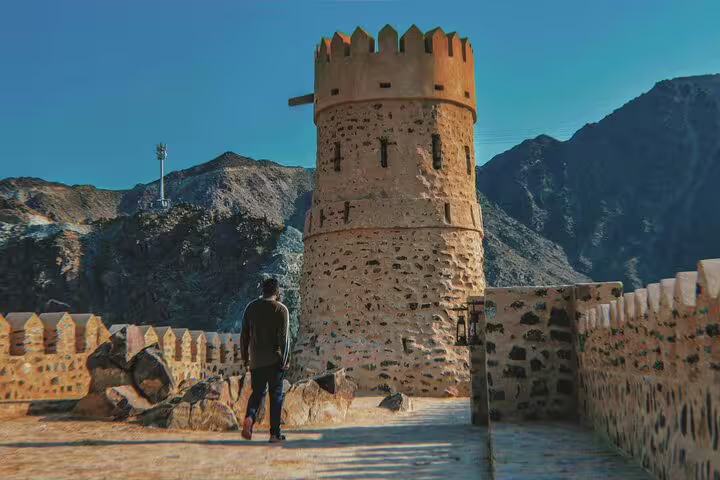 Traveler exploring a historic stone fort against a mountainous backdrop on a Six Emirates tour from Dubai.