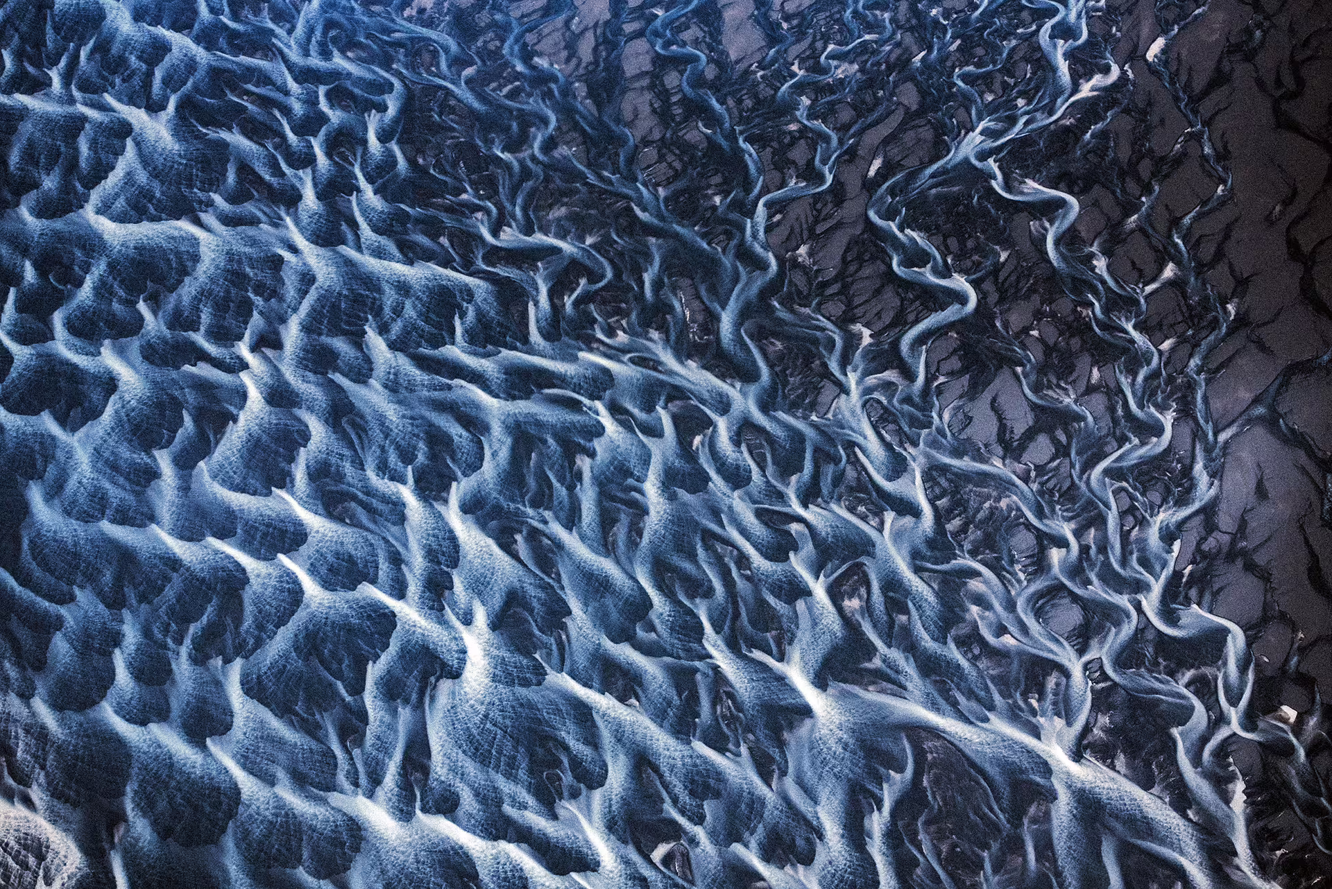 Aerial view of glacial river braids with blue water channels flowing across dark volcanic sand in Skaftafell Iceland