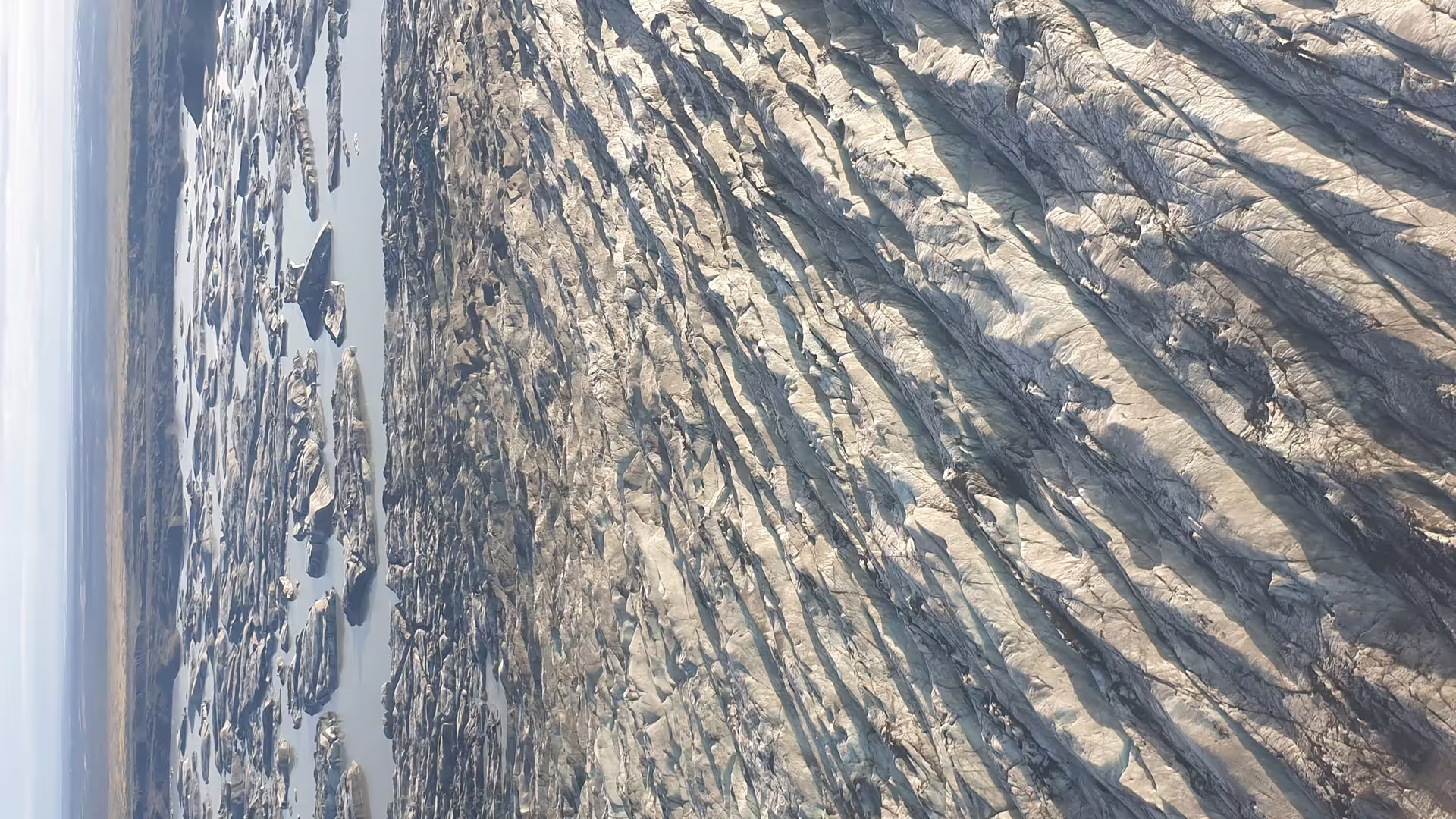 Aerial view of Skaftafell glacier surface with parallel crevasse ridges and meltwater pools below