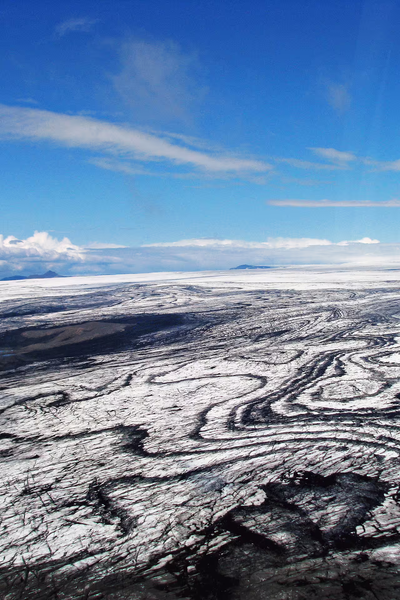 Aerial view of Skaftafell glacier with dark moraine patterns and snow-covered ice cap under blue sky