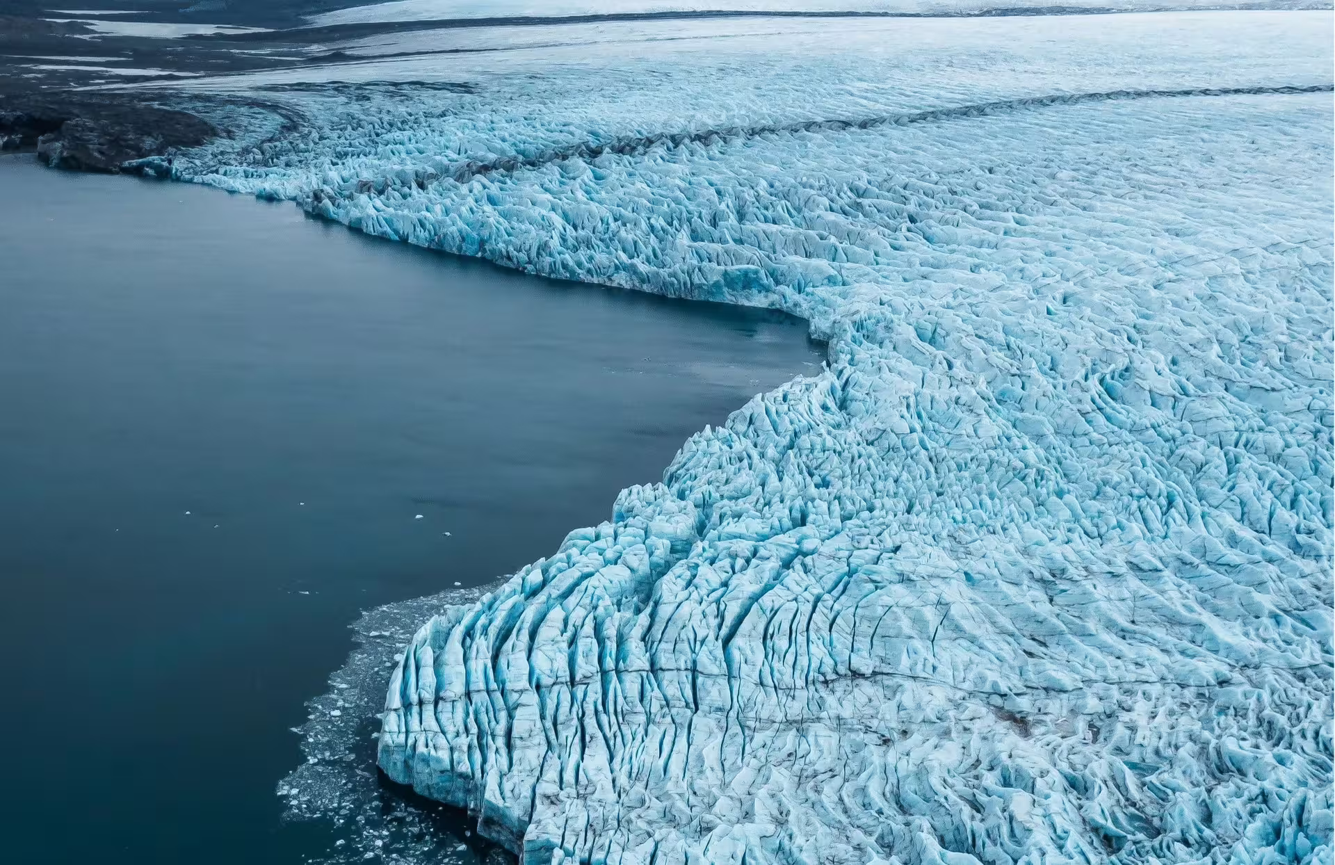 Aerial view of a glacier meeting turquoise water in Skaftafell, Iceland, with jagged blue ice formations