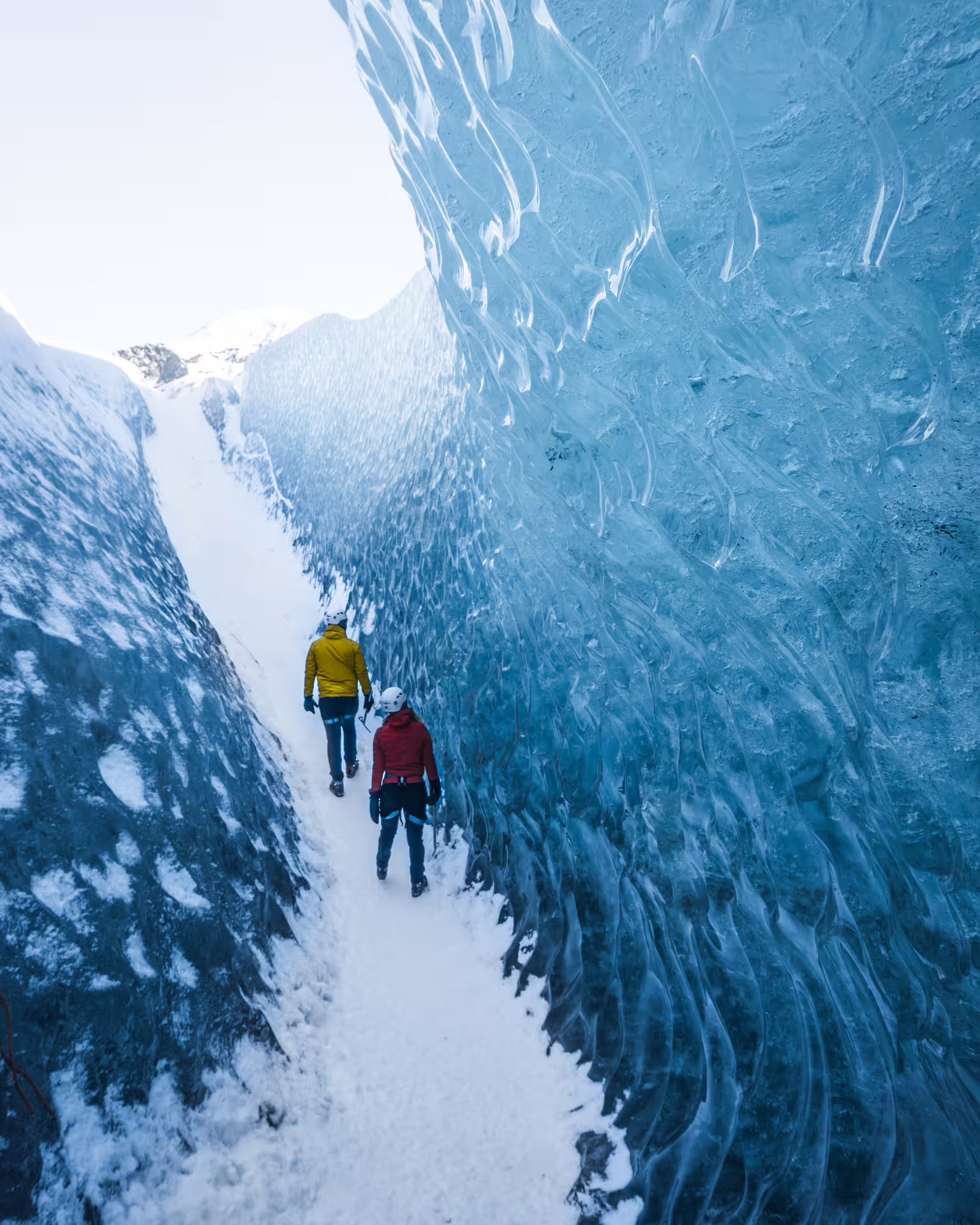 Two hikers walking through a narrow blue ice cave corridor at Skaftafell glacier