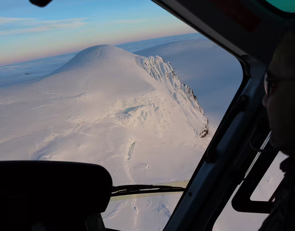 Aerial helicopter view of snow-covered glacier and mountain peaks in Skaftafell, Iceland at sunset