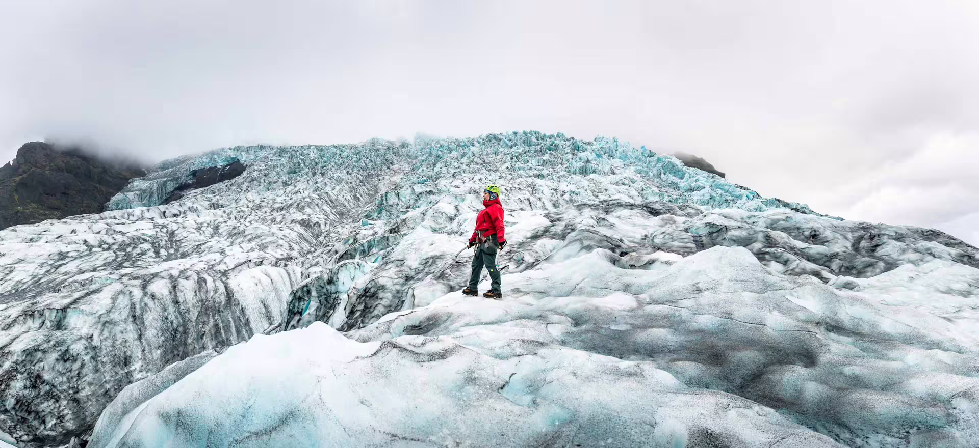 Guide in red jacket standing on Skaftafell glacier ice field with jagged blue ice formations and misty mountains behind