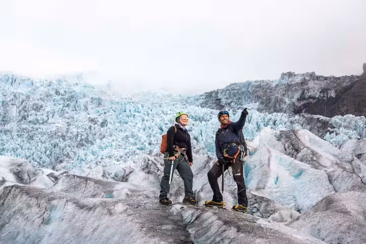 Two hikers with ice axes and helmets standing on Skaftafell glacier with blue ice formations behind them