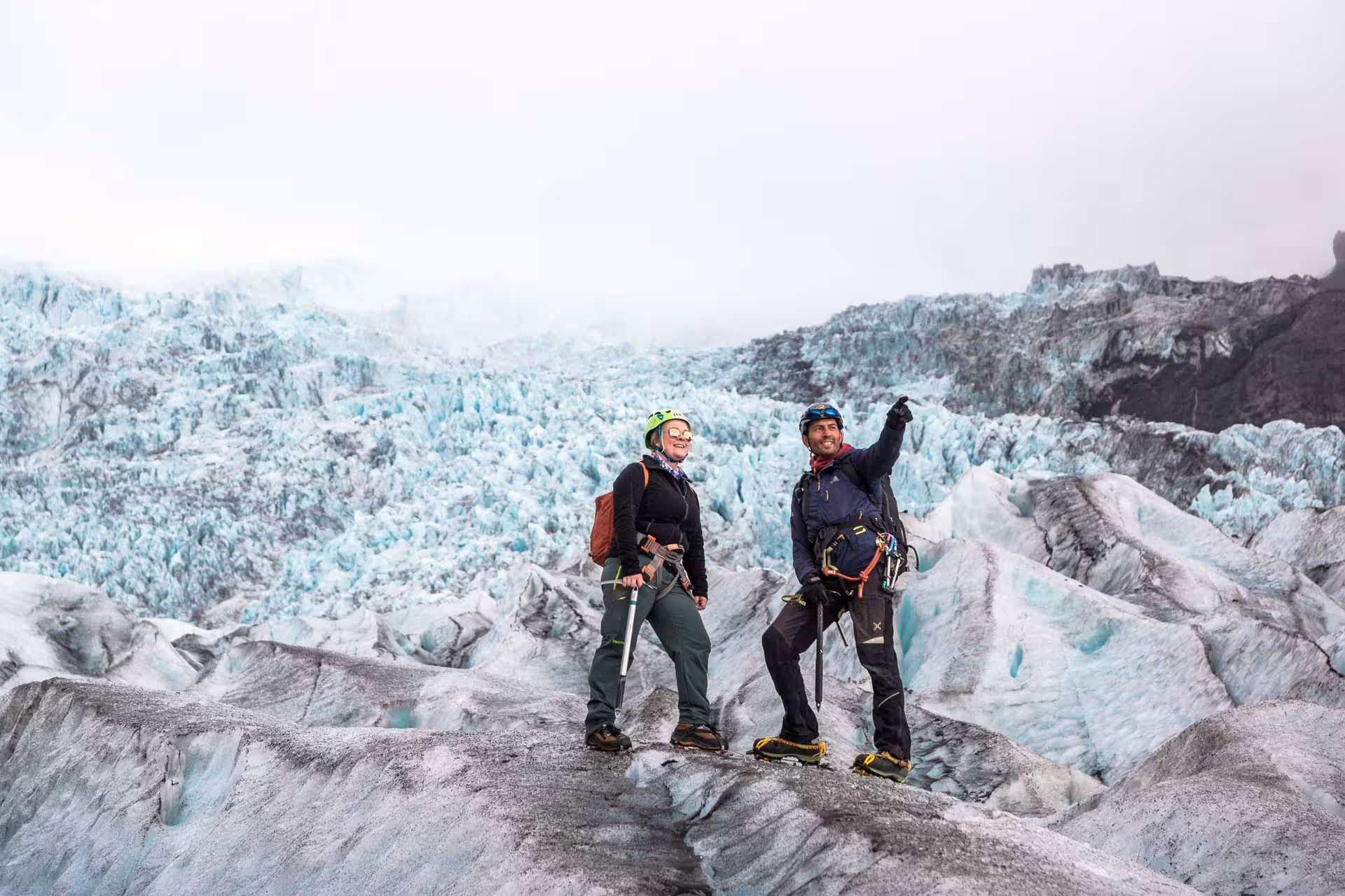 Two hikers with ice axes and helmets standing on Skaftafell glacier with blue ice formations behind them