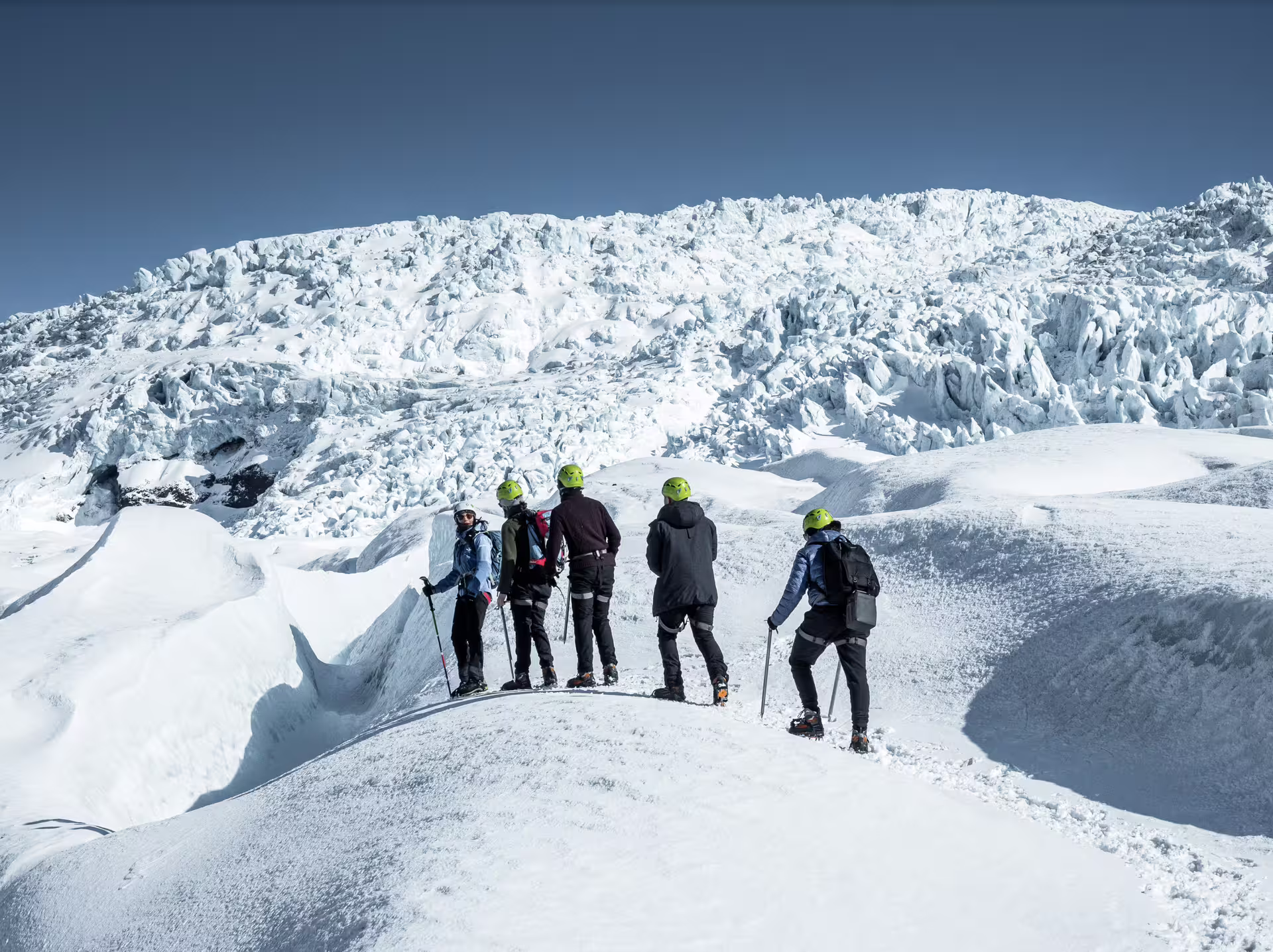 Group of hikers with green helmets and crampons exploring Skaftafell glacier surrounded by ice formations