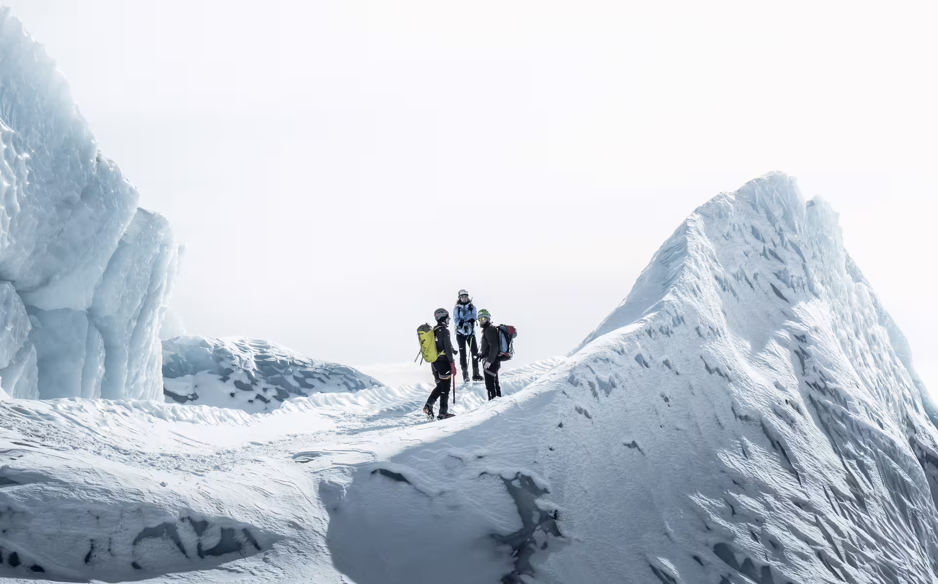 Three mountaineers with backpacks navigating icy glacier terrain surrounded by towering snow formations at Skaftafell