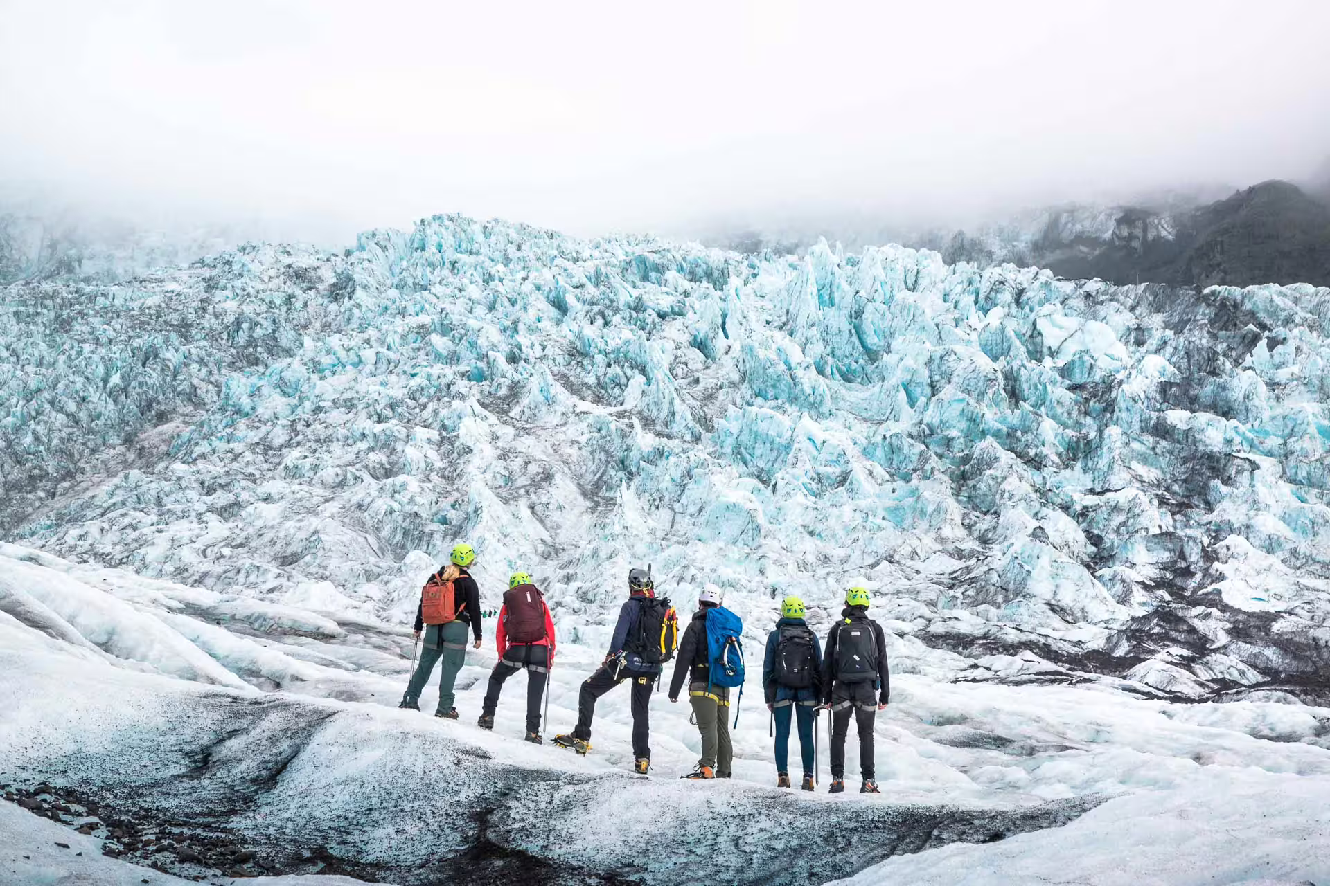 Group of hikers in helmets and backpacks standing on Skaftafell glacier surveying blue ice formations