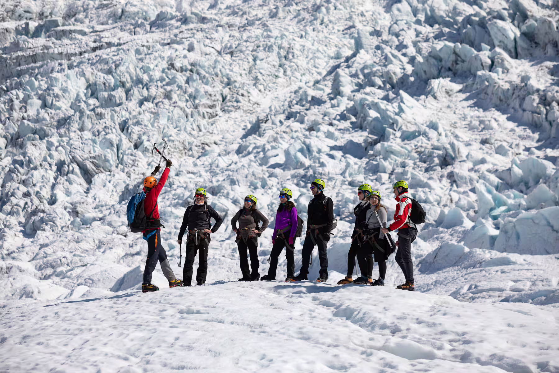 Guide demonstrating ice axe use to a group of hikers with helmets and crampons on Skaftafell glacier