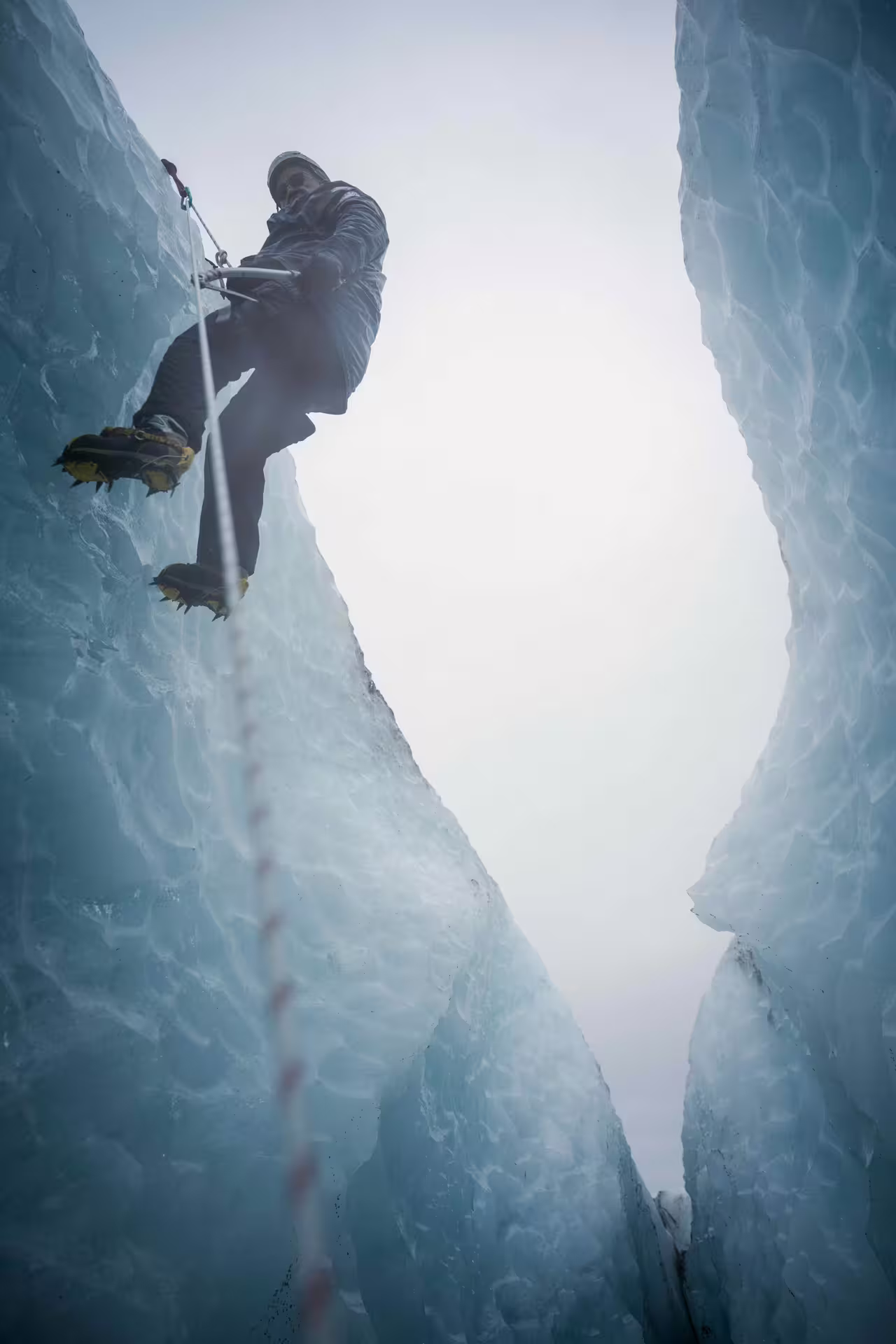 Climber with crampons and ice axe ascends a dramatic glacial crevasse on a guided Skaftafell Iceland ice climbing tour.