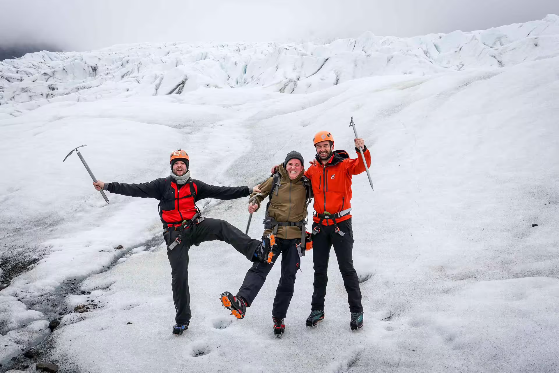 Three happy ice climbers celebrate with ice axes on the vast Skaftafell glacier during a guided ice climbing tour in Iceland.
