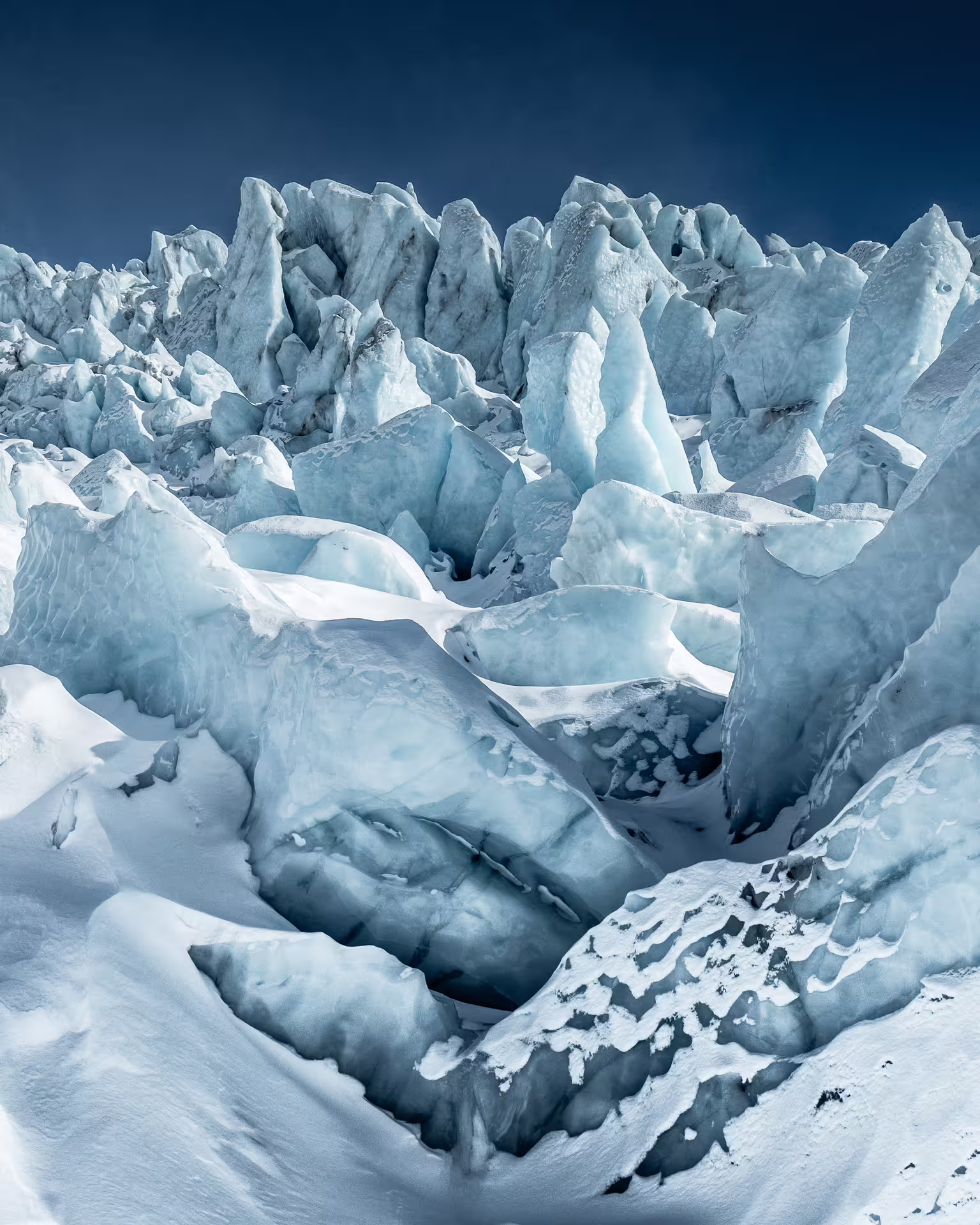 Jagged blue ice formations and deep crevasses on Skaftafell glacier under a clear blue sky