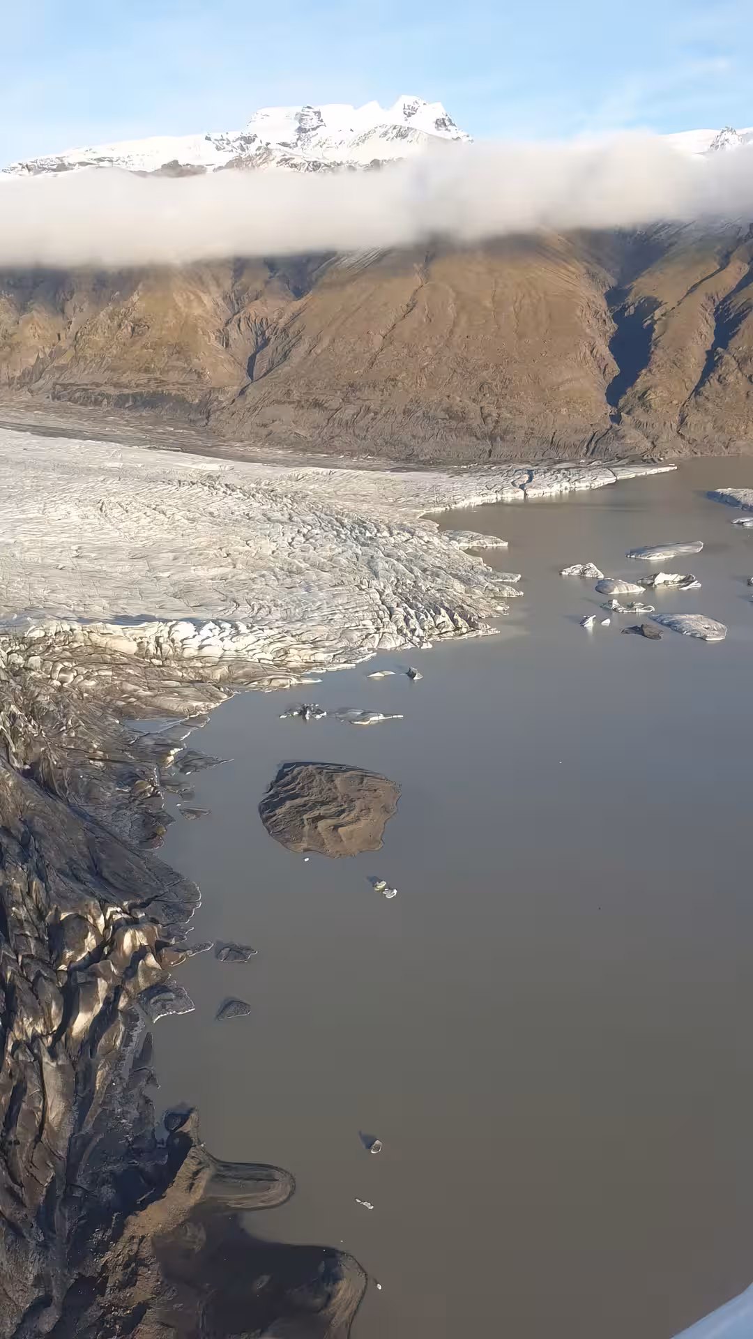 Aerial view of Skaftafell glacier tongue meeting a glacial lagoon with icebergs and snow-capped mountains behind