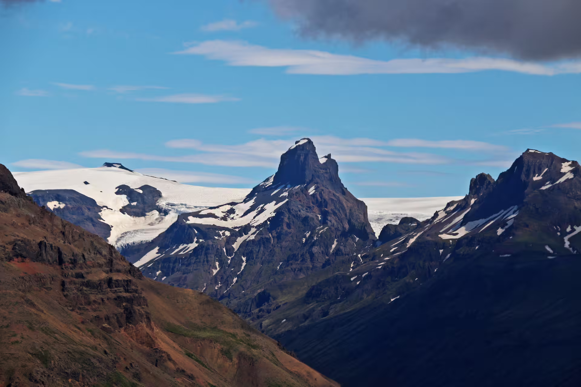Dramatic rocky mountain peak with glaciers and snow-covered plateaus under blue sky in Skaftafell Iceland