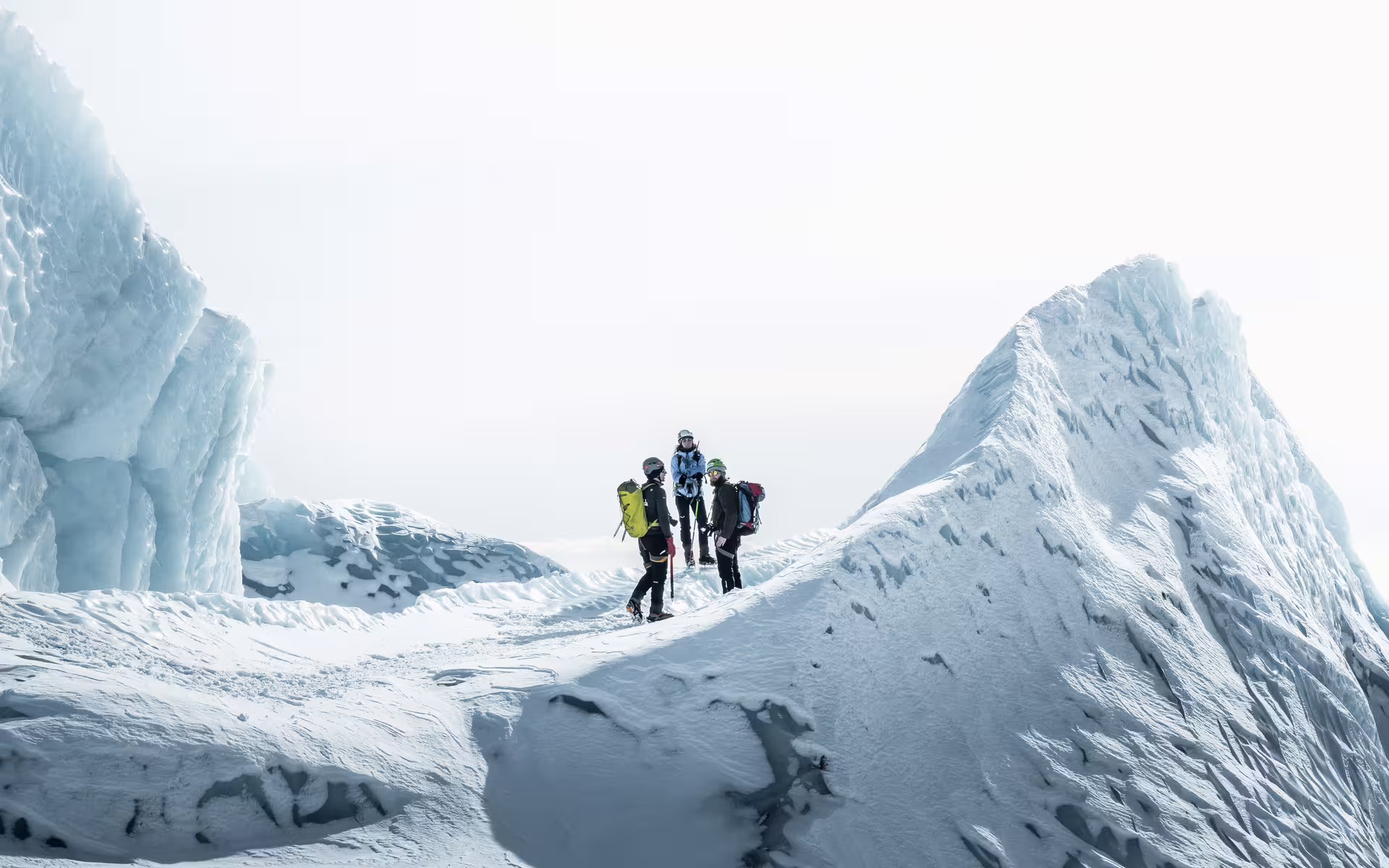 Three mountaineers with backpacks navigating a snowy glacier between large ice formations in Skaftafell