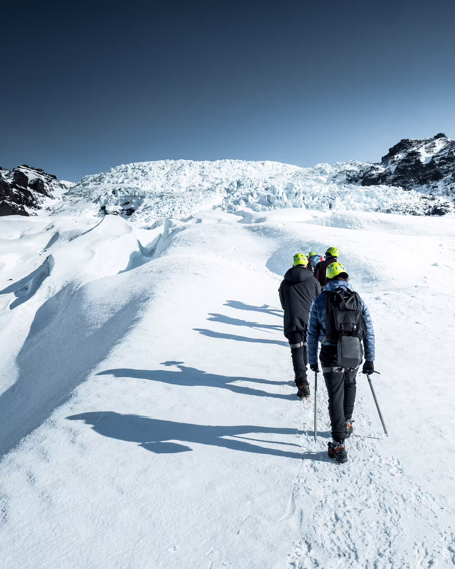 Group of hikers in yellow helmets trekking across Skaftafell glacier with ice formations ahead