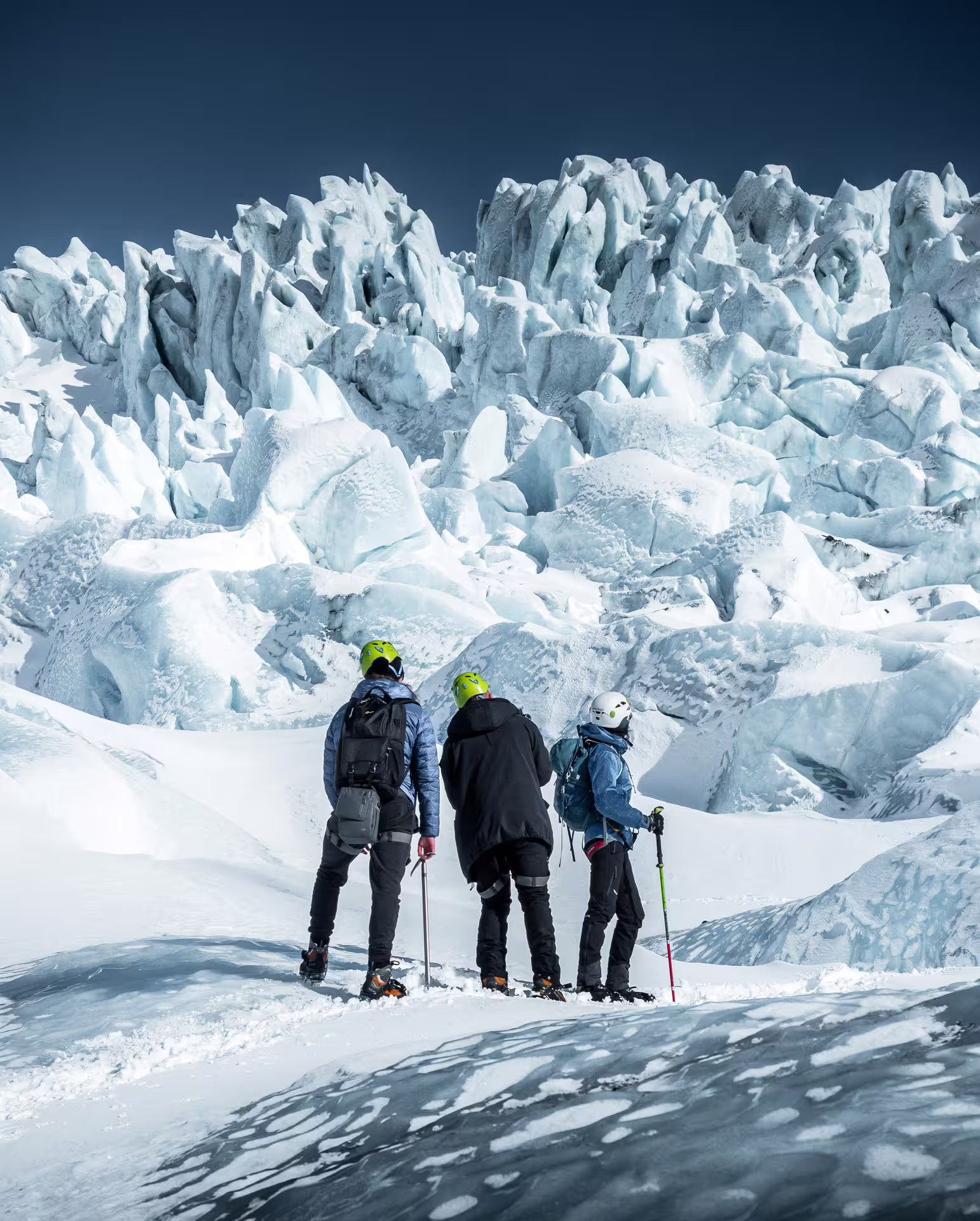 Three hikers with helmets and poles standing before jagged glacial ice formations at Skaftafell glacier