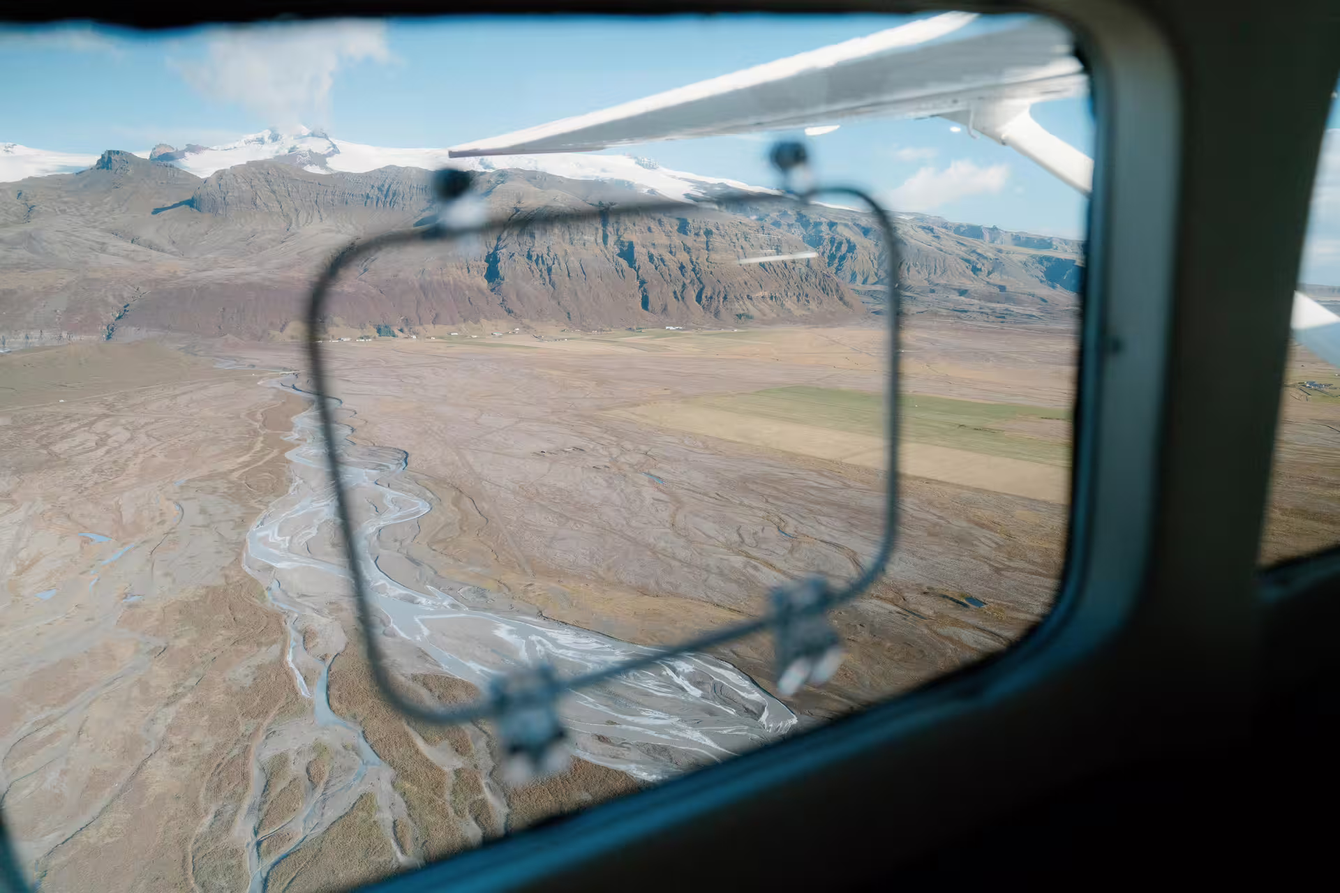 Aerial view of braided glacial rivers and black sand plains from small plane window over Skaftafell