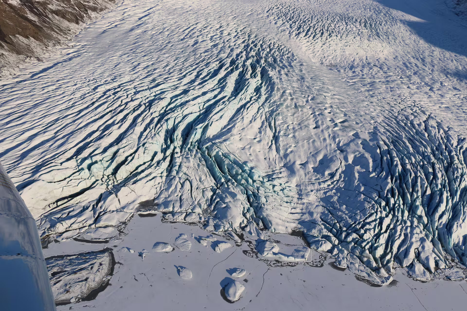 Aerial view of Skaftafell glacier with deep blue crevasses and ice formations flowing toward frozen plains