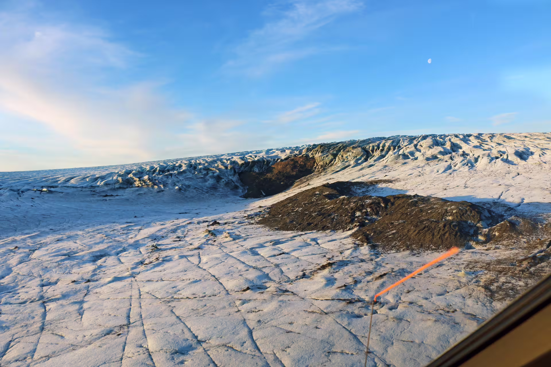 Aerial view of Skaftafell glacier with cracked ice fields, dark volcanic rock, and blue sky from scenic flight