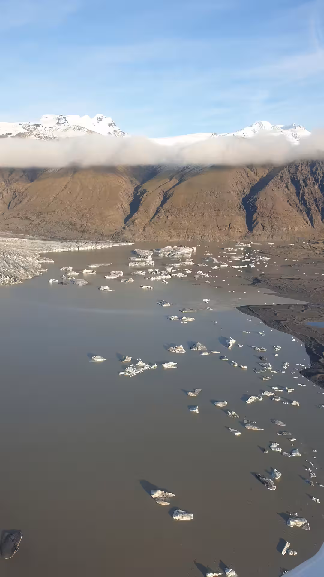 Aerial view of glacier lagoon with floating icebergs, rugged mountains, and snow-capped peaks in Skaftafell, Iceland