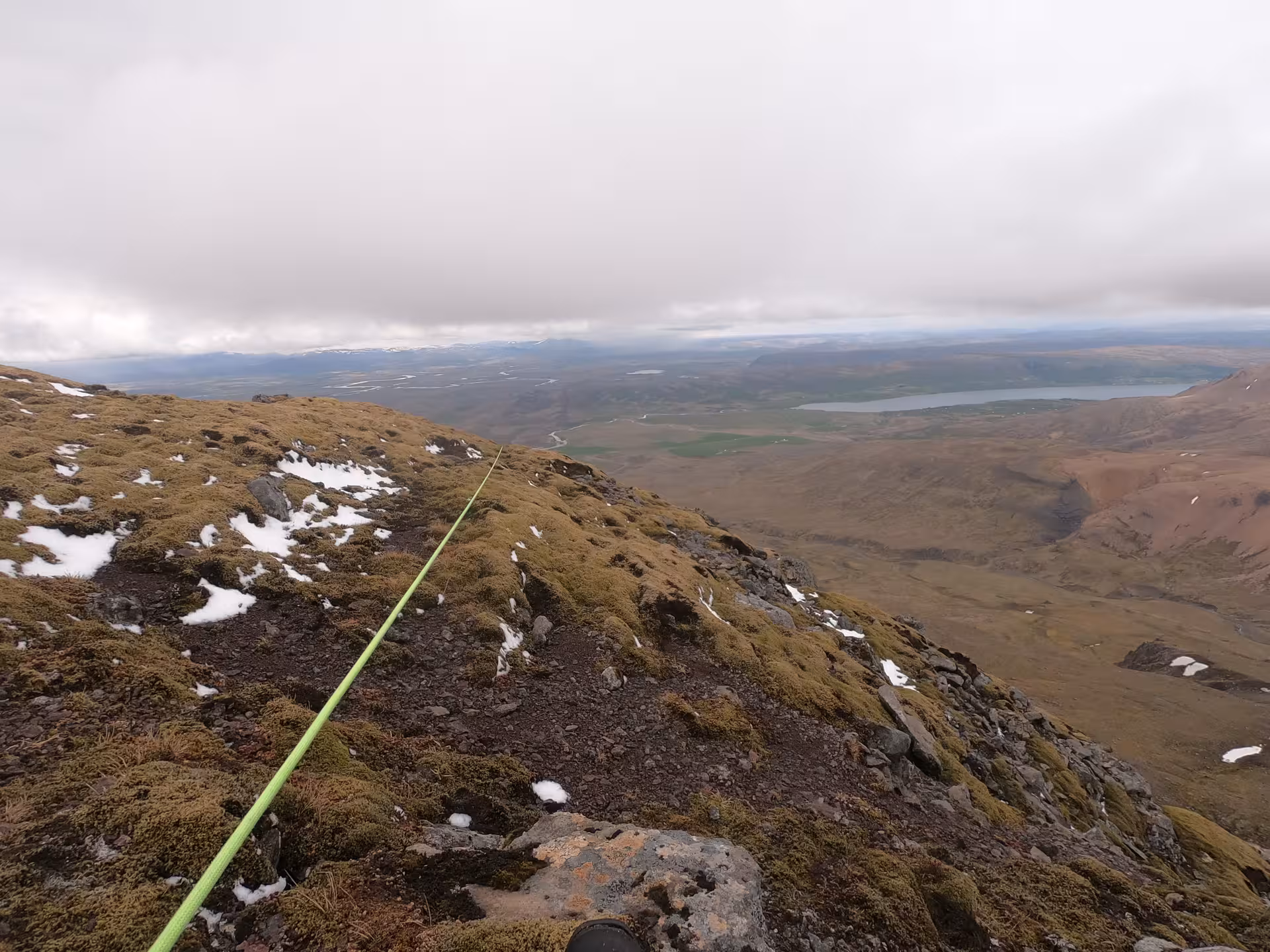 Green climbing rope on mossy rocky ridge of Skessuhorn mountain with lake and valley views below