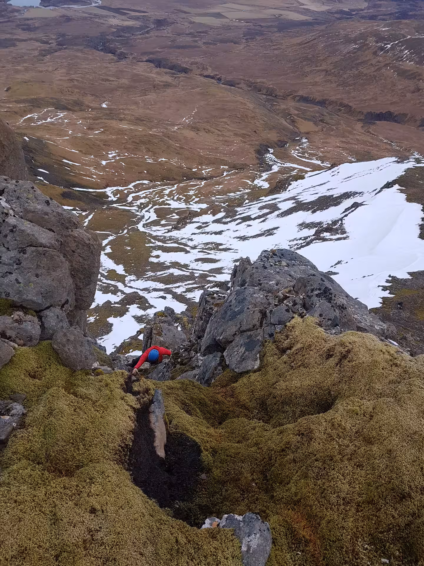 Climber in red jacket scaling rocky ridge on Skessuhorn alpine mountain with snowy valley below