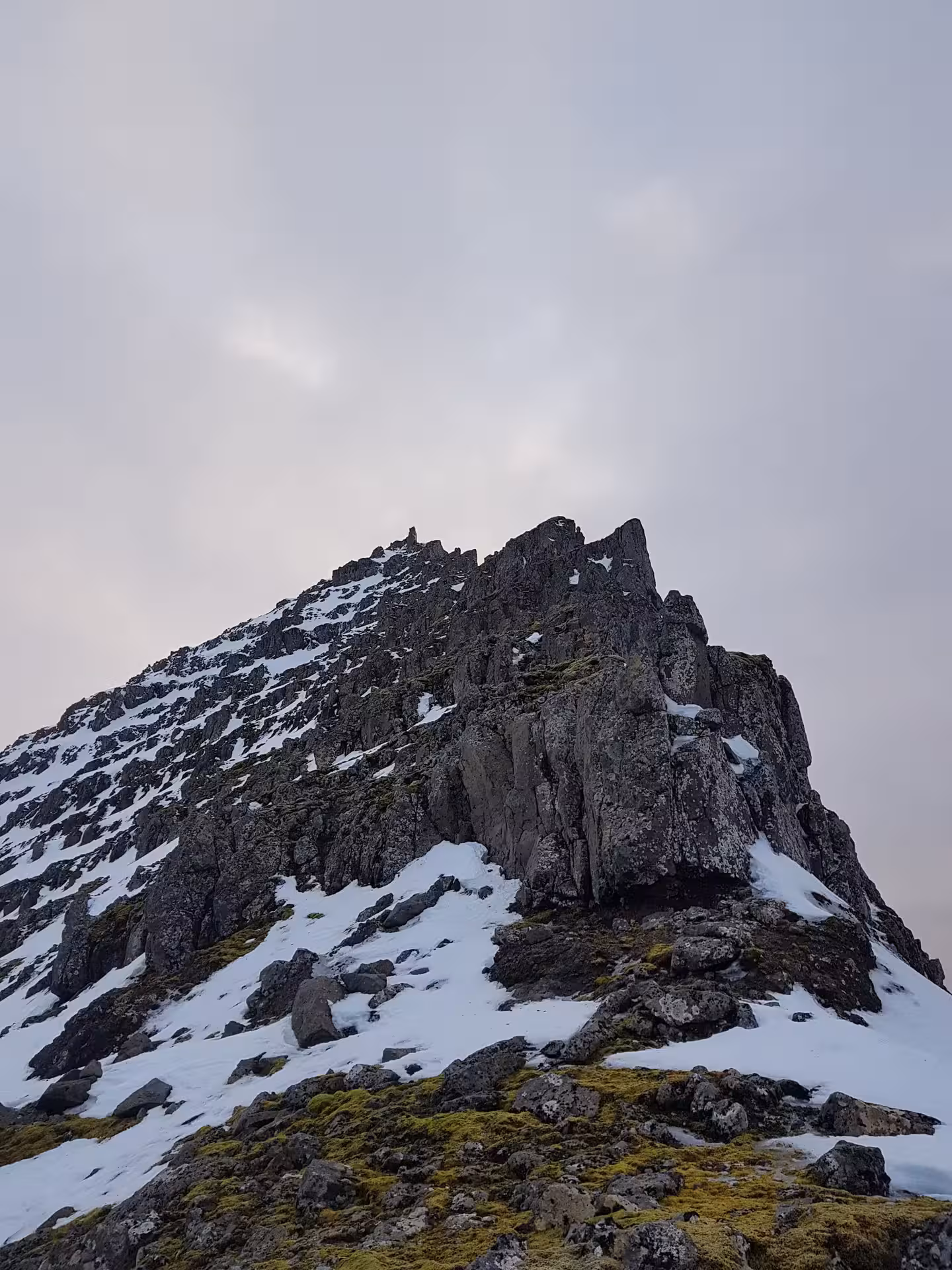 Rocky snow-covered summit of Skessuhorn alpine mountain under overcast sky
