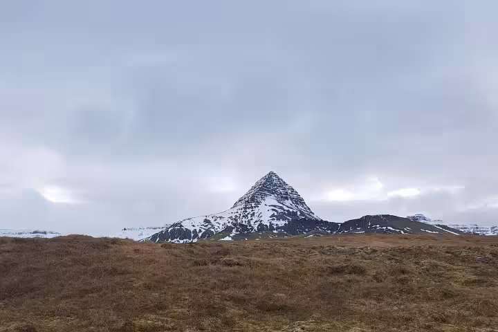 Snow-capped Skessuhorn mountain with pyramid peak rising above brown moorland under overcast sky